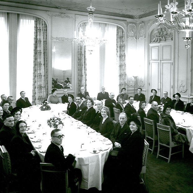 Historic black and white photograph of a formal banquet at Claridge’s, with guests seated around a long table in an ornate dining room.