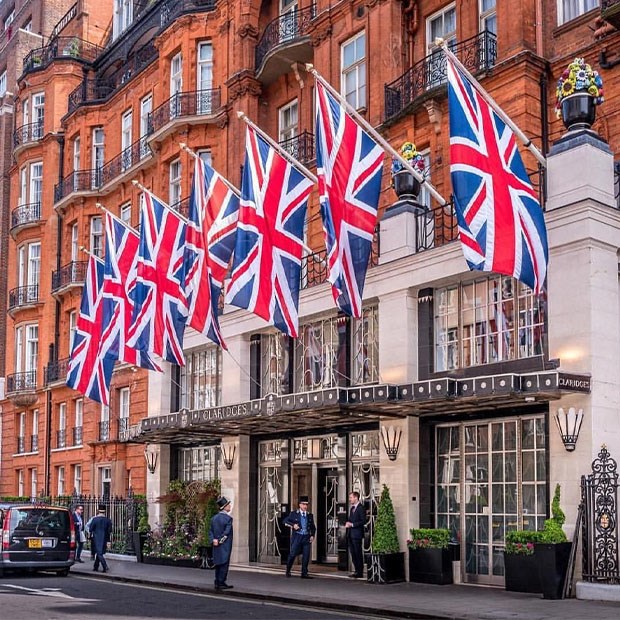 Claridge’s hotel exterior with multiple Union Jack flags displayed above the entrance, with doormen standing outside.