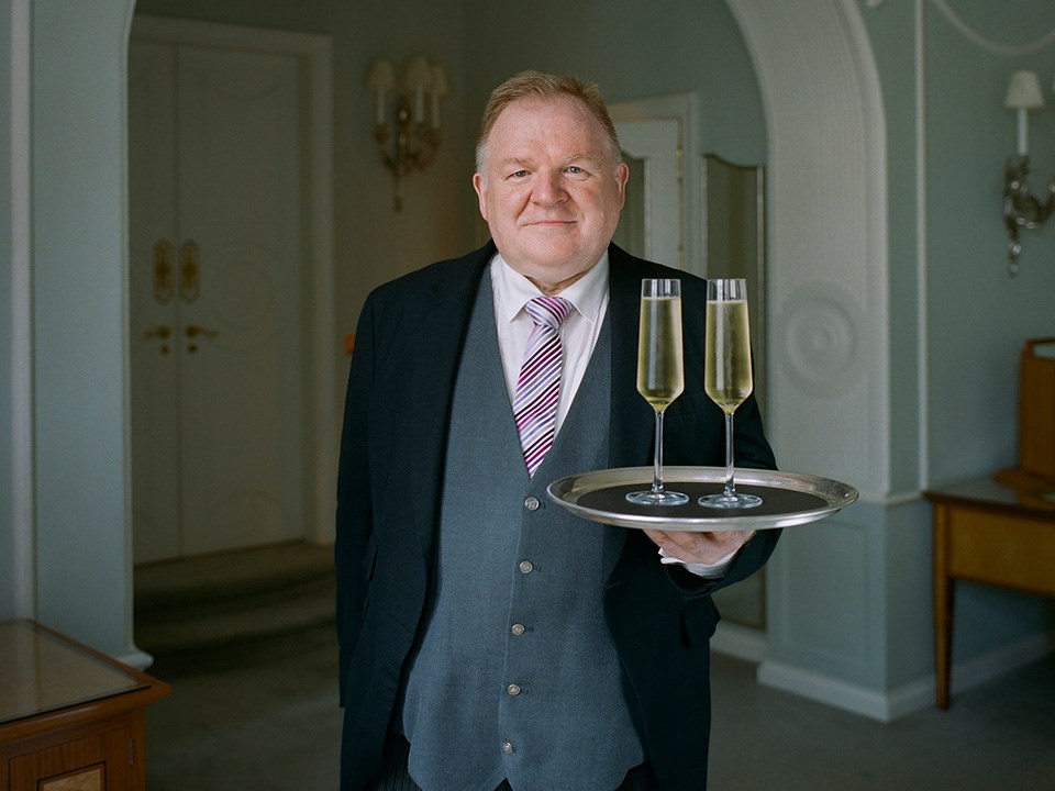 Claridge's butler Michael Lynch carrying two glasses of champagne on a tray to his guests.