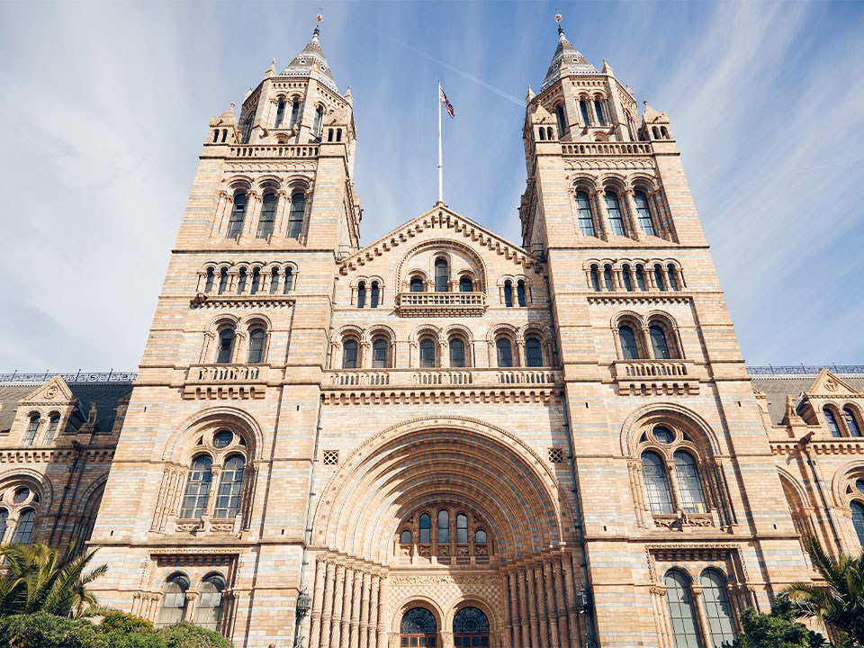 View of the front of the National History Museum, an impressive building with blue sky in the background.