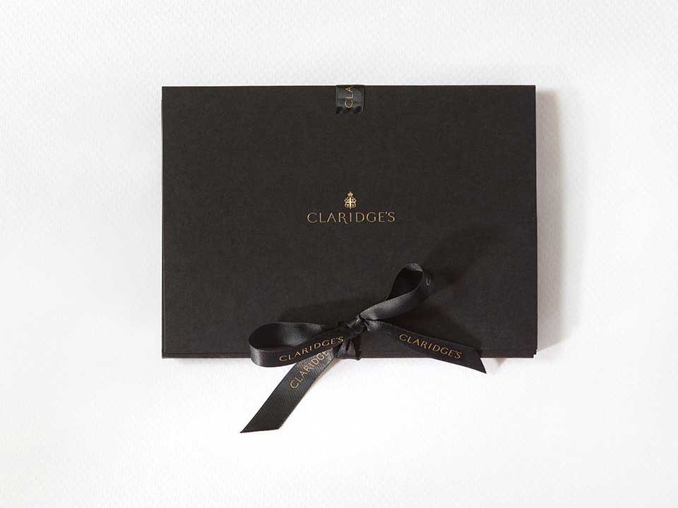 Presentation of a luxurious gift voucher to experience Claridge's, with an elegant black bow.