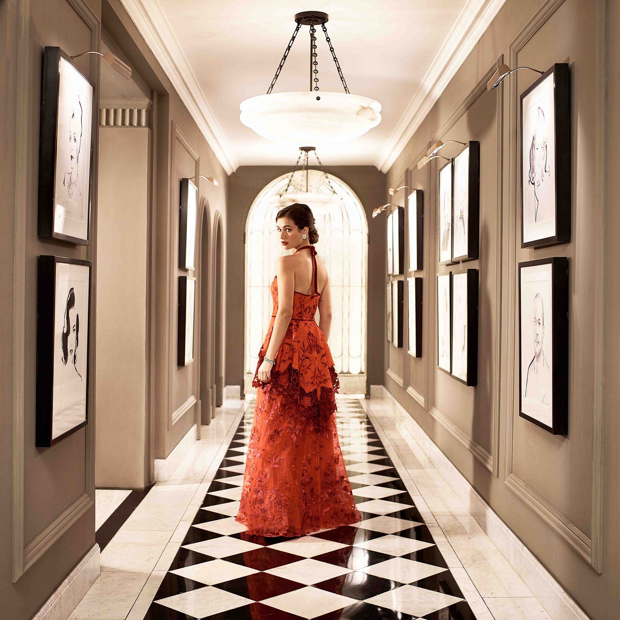 A girl in a red dress looking from the back in the corridor of Claridge's Hotel, in an art deco interior design.