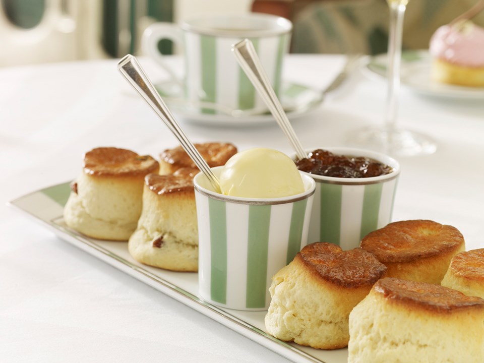 Delicious scones with jam and clotted cream, served on a mint green and white plate.