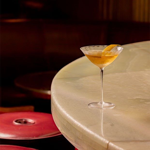 A perfectly crafted cocktail rests elegantly on a marble bar, illuminated by warm ambient lighting.
