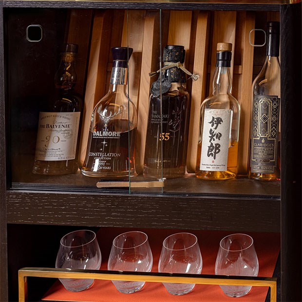 A luxurious display of rare and premium whisky bottles showcased in a glass cabinet with exquisite glassware below.