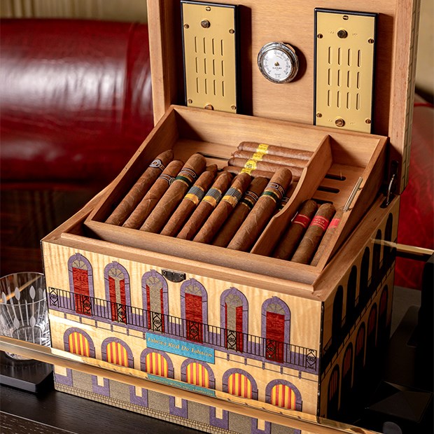 A beautifully crafted humidor, adorned with vibrant architectural designs, displays an exquisite selection of premium cigars in a luxurious bar setting.