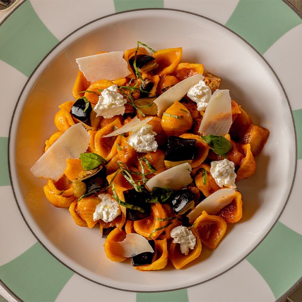 Colourful pasta with ricotta, aubergine, and fresh herbs on a green-rimmed plate.