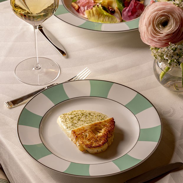 Roasted cauliflower steak with a creamy herb sauce, served on a green-rimmed plate.