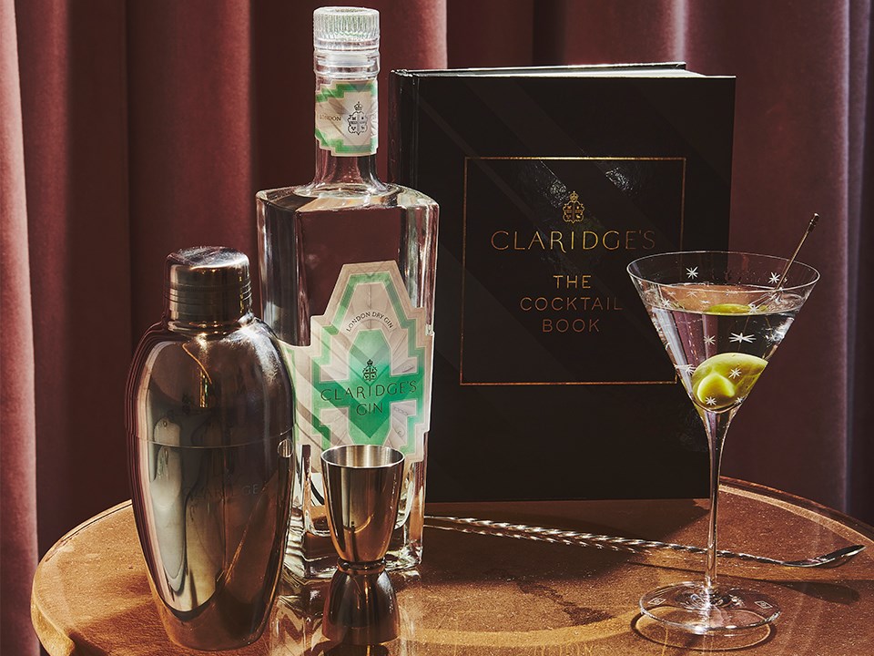 Presentation of Claridge's Gin, Cocktail Book, shaker, and martini glass with drink and olive.