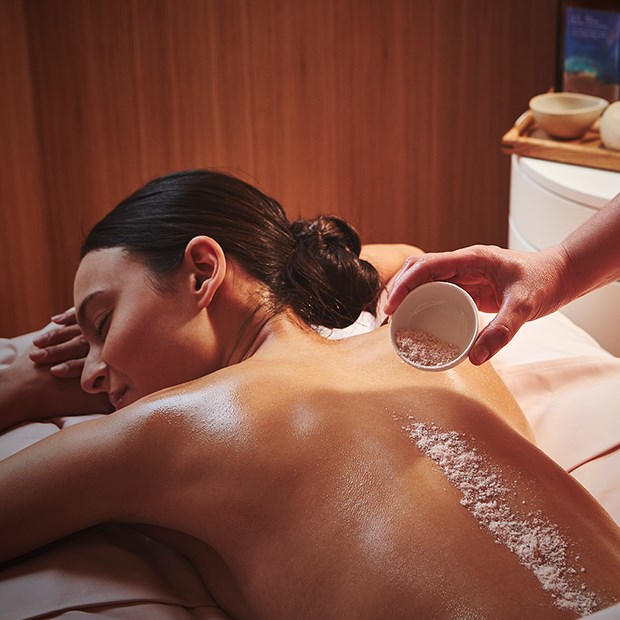 A view of a woman enjoying a massage and spa treatment at Claridge's Spa, and a person pouring the treatment over her back.