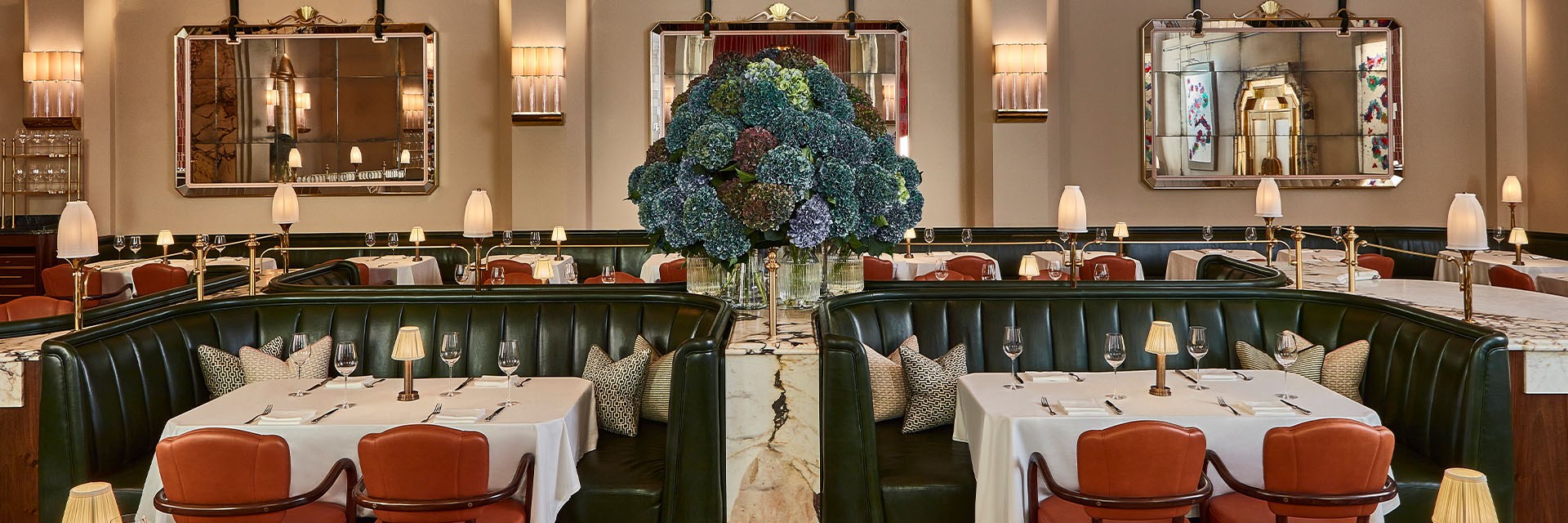 Claridge's restaurant with green banquets, set tables and a big vase of blue hydrangeas in the centre