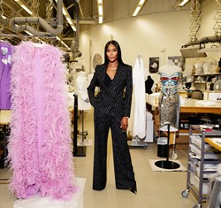 Naomi in pin striped suite in an atelier with clothes around her