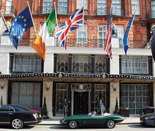 A view of the entrance outside Claridge's Hotel, with doorkeeper, flags and parked cars outside.