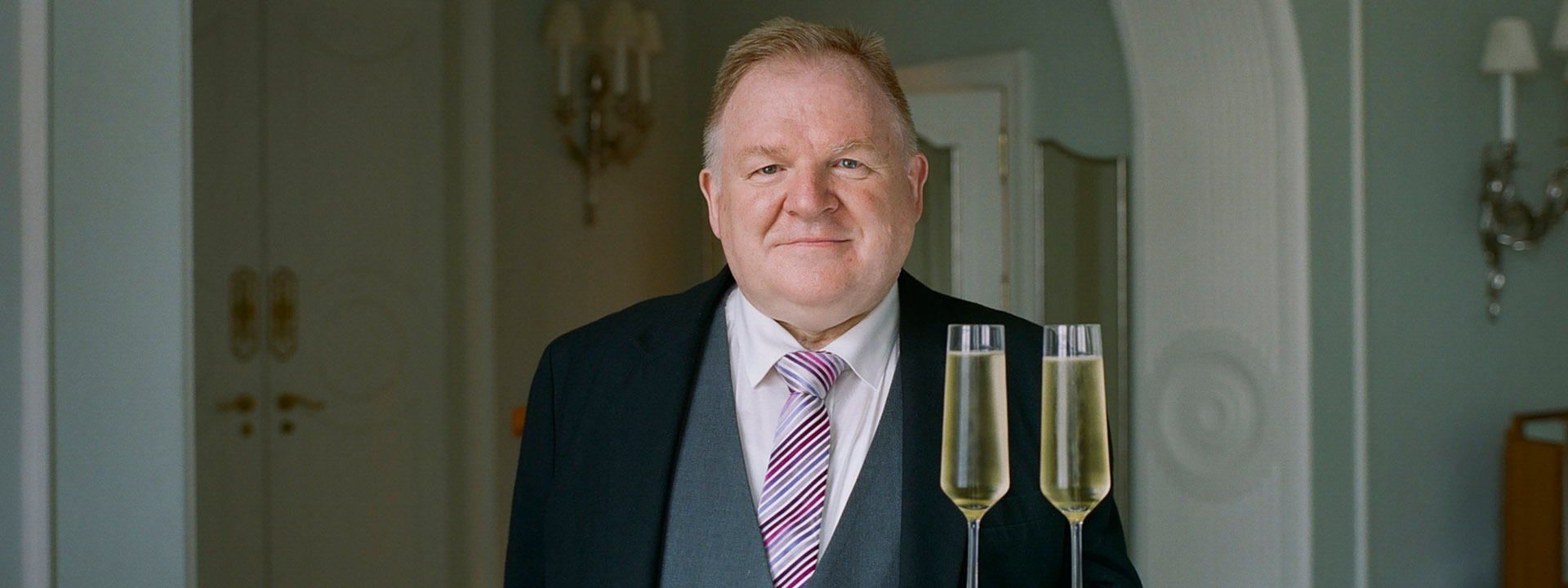 Claridge's butler Michael Lynch carrying two glasses of champagne on a tray to his guests.