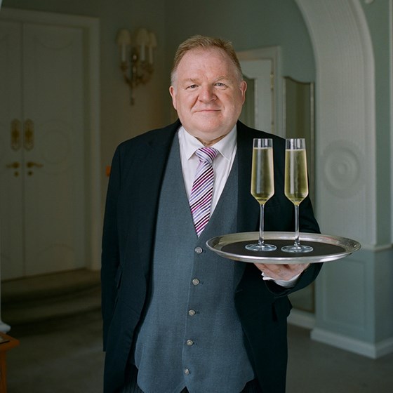 Claridge's butler Michael Lynch carrying two glasses of champagne on a tray to his guests.