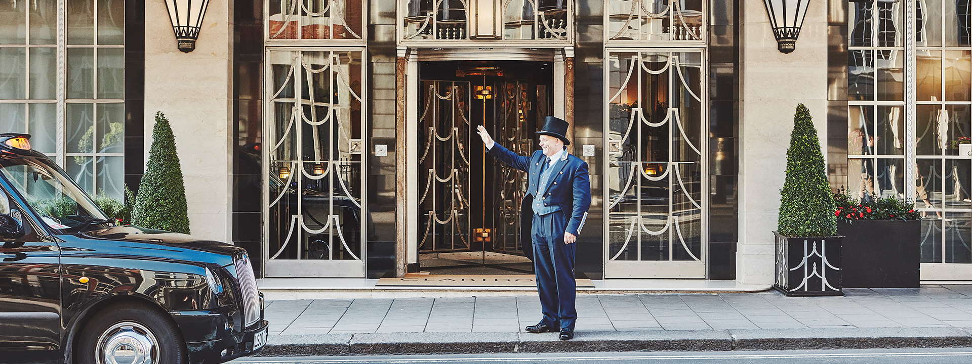 The doorman waves warmly and welcomes guests outside the entrance of Claridge's Hotel.