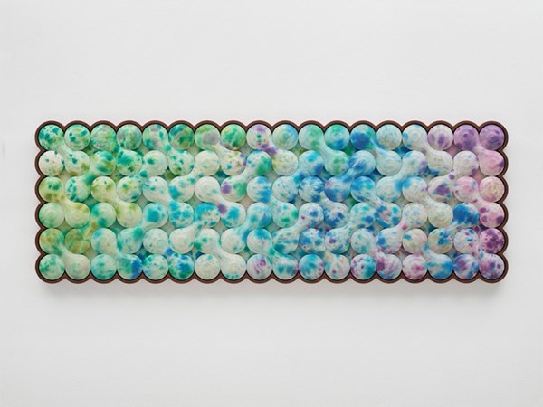Close-up of abstract artwork with repeating rounded shapes in soft blue, green, and purple tones, framed by a brown scalloped edge against a white background.