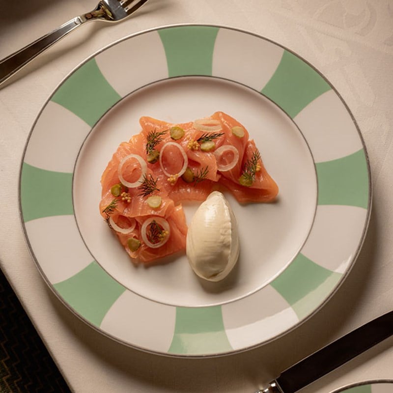 A delicate plate of cured salmon, garnished with fresh dill and thinly sliced onions, accompanied by a quenelle of cream on a stylish plate.