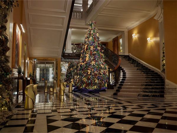 Grand Christmas tree adorned with colourful Burberry ribbons and lights in Claridge’s Art Deco lobby, framed by sweeping staircases.