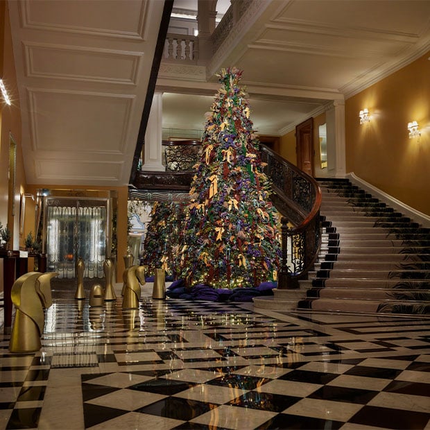 Claridge’s lobby with towering Burberry Christmas tree, marble staircase and gold chess-piece sculptures on chequered floor.