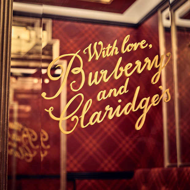 Gold script reading “With love, Burberry and Claridge’s” on mirrored panel against red tartan walls.