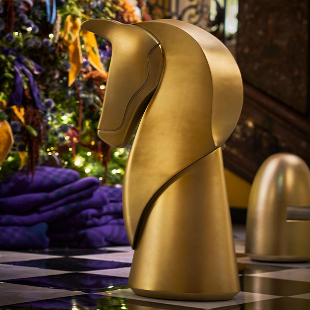 Large sculptural gold chess knight in Claridge’s lobby, with blurred Burberry Christmas tree lights behind.