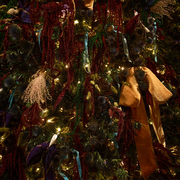 Close-up of Burberry-designed Christmas tree at Claridge’s, dense with velvet ribbons, foliage and warm fairy lights.