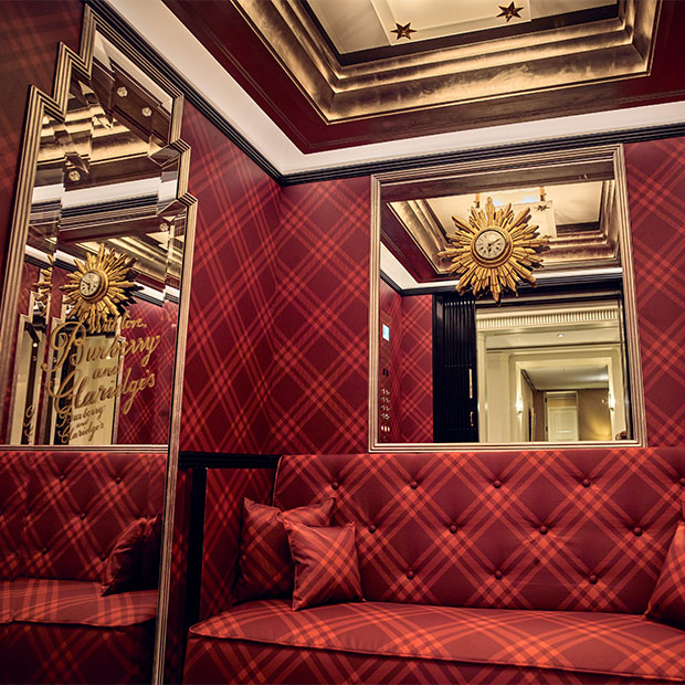 Red tartan-lined Claridge’s alcove with mirrored panels, cushioned bench seating and decorative sunburst clock.