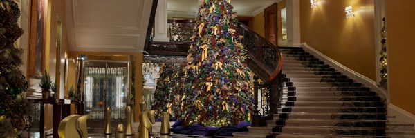 Wide view of Claridge’s lobby with Burberry Christmas tree, sweeping marble staircase and gold chess-piece sculptures.