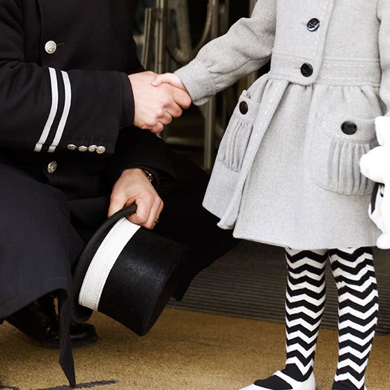 A view of a butler shaking hands with a girl holding a teddy bear outside Claridge's.