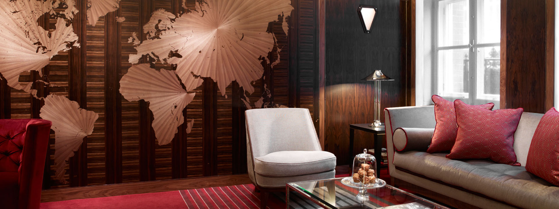 A view of the Claridge's Map Room wall and armchair with a comfortable sofa in shades of red.