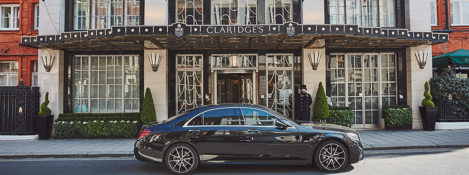 Display of a car in front of the entrance of Claridge's Hotel as well as a friendly doorman.