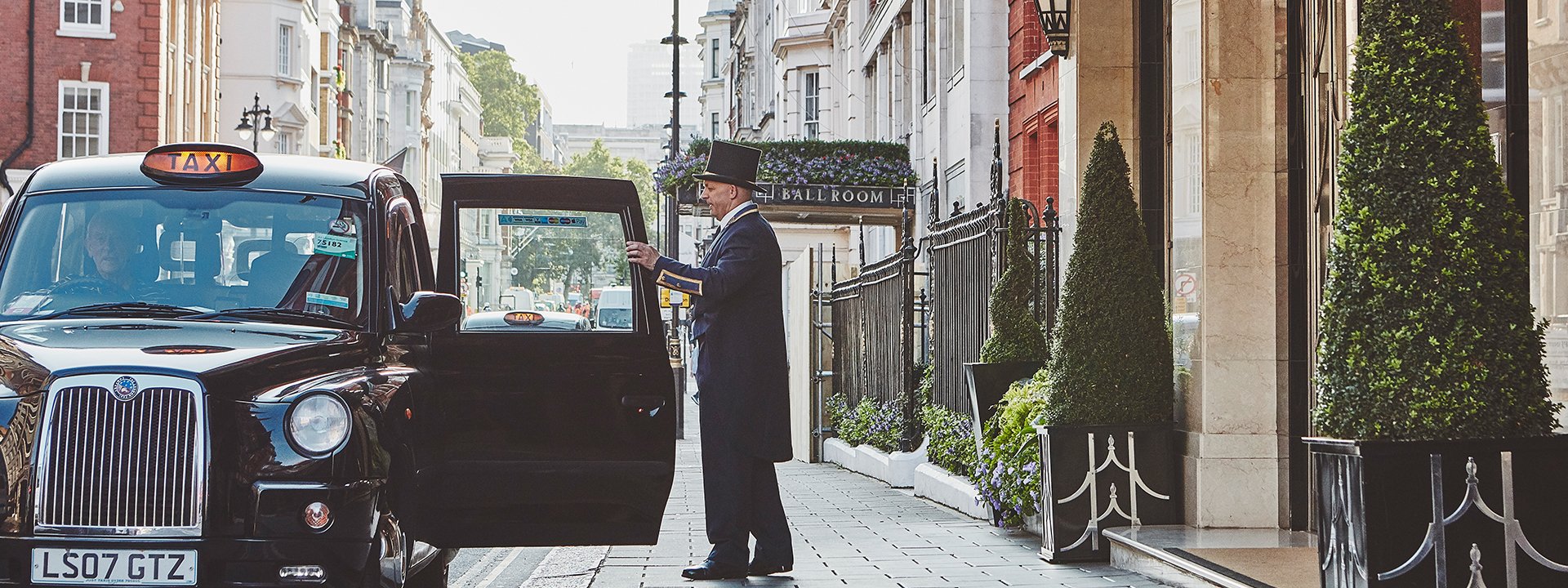 A doorman who opens the door of a taxi outside Claridge's Hotel and welcomes guests.