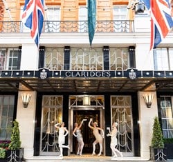 Dancers in flapper-style costumes posing under the entrance of Claridge’s with Union Jack flags fluttering in the breeze.