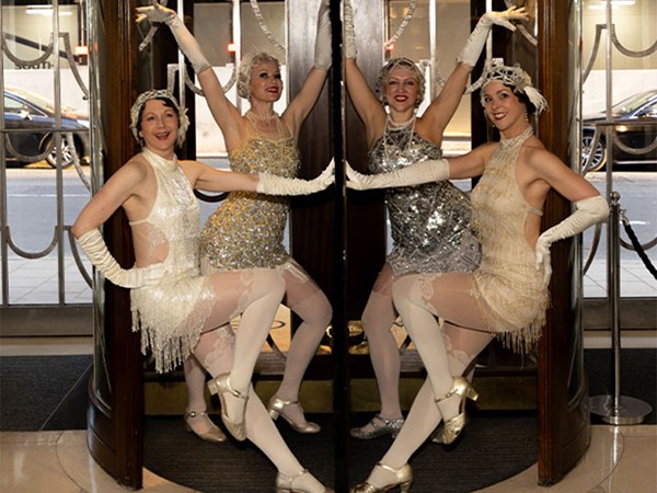 Four women in 1920s-style flapper dresses pose in a revolving door at Claridge’s entrance.