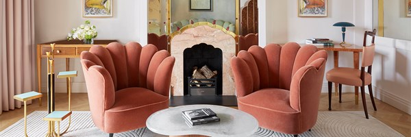 Two scalloped velvet chairs facing fireplace with mirrored Art Deco detailing and pastel art.