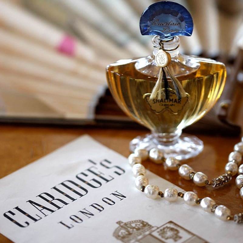 Guerlain Shalimar perfume bottle beside Claridge’s London card and pearl necklace.