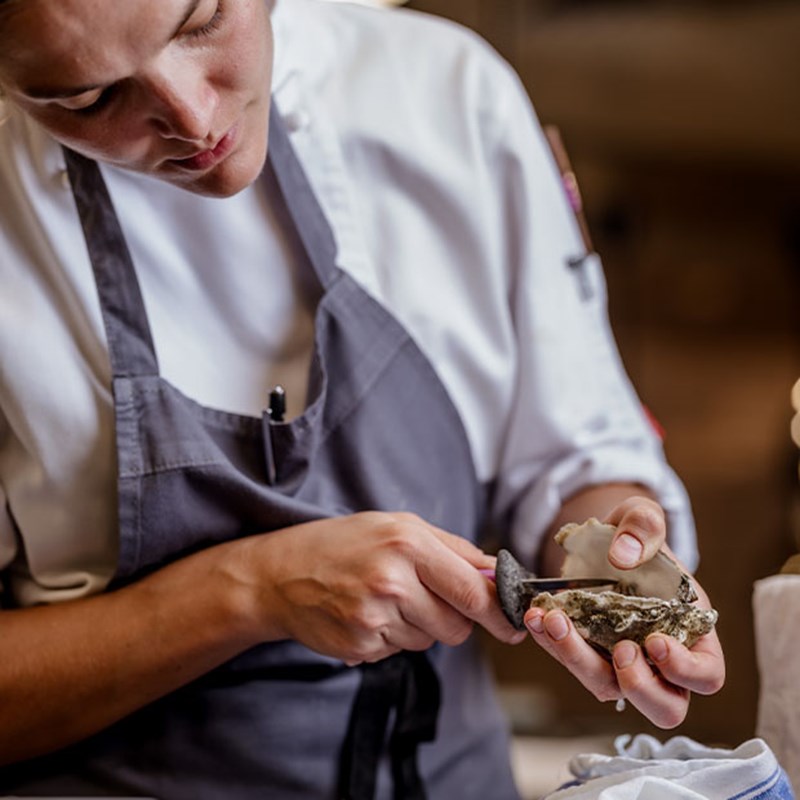 A focused chef carefully shucks an oyster, revealing its delicate, briny flesh, in preparation for an elegantly plated seafood dish.