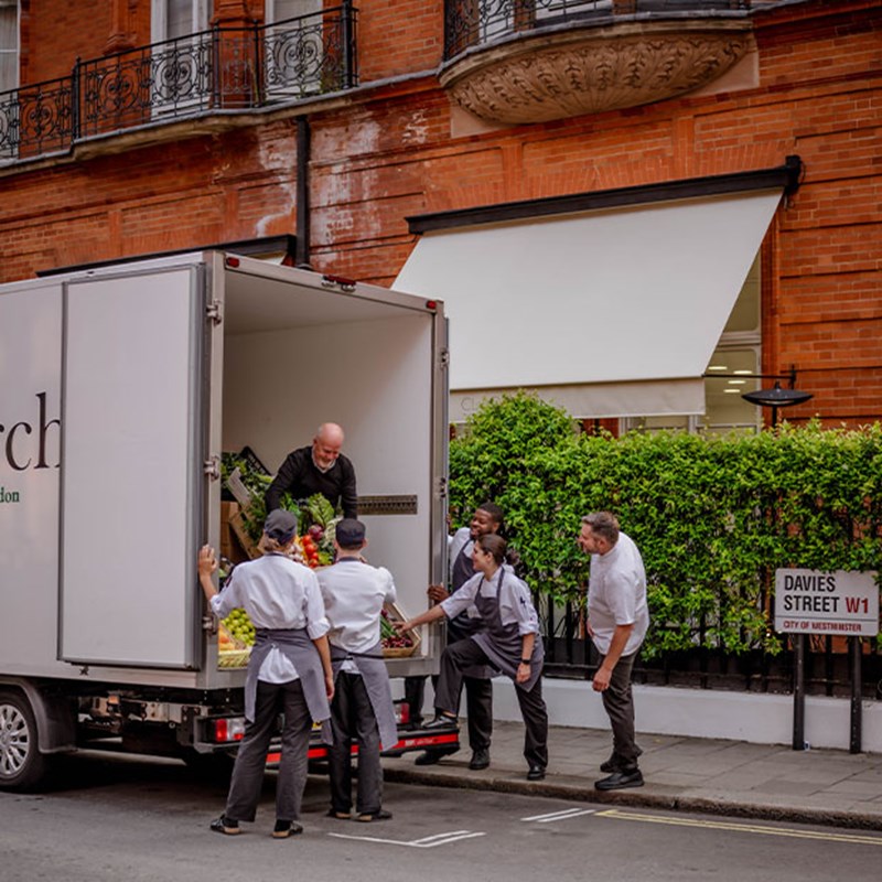 A team of chefs gathers around a delivery truck on Davies Street, receiving an abundant selection of seasonal produce from a trusted supplier.