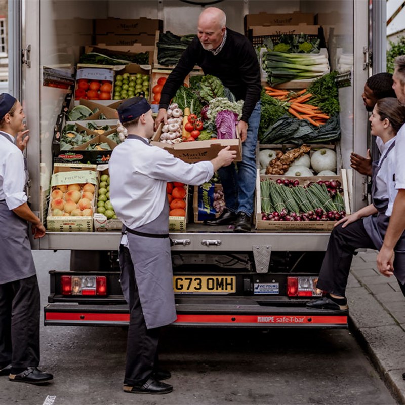 Chefs work together to unload a delivery of crates stacked with fresh fruits, vegetables, and herbs, a testament to Claridge’s commitment to quality ingredients.