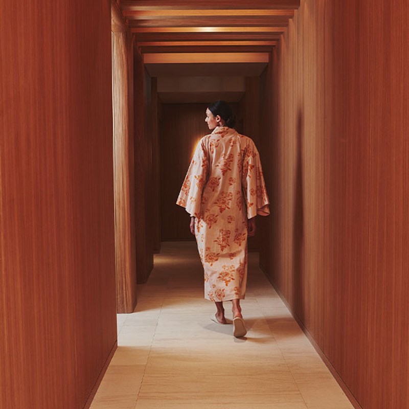 Woman with dark hair in pink printed kimono walking down the Claridge's spa corridor