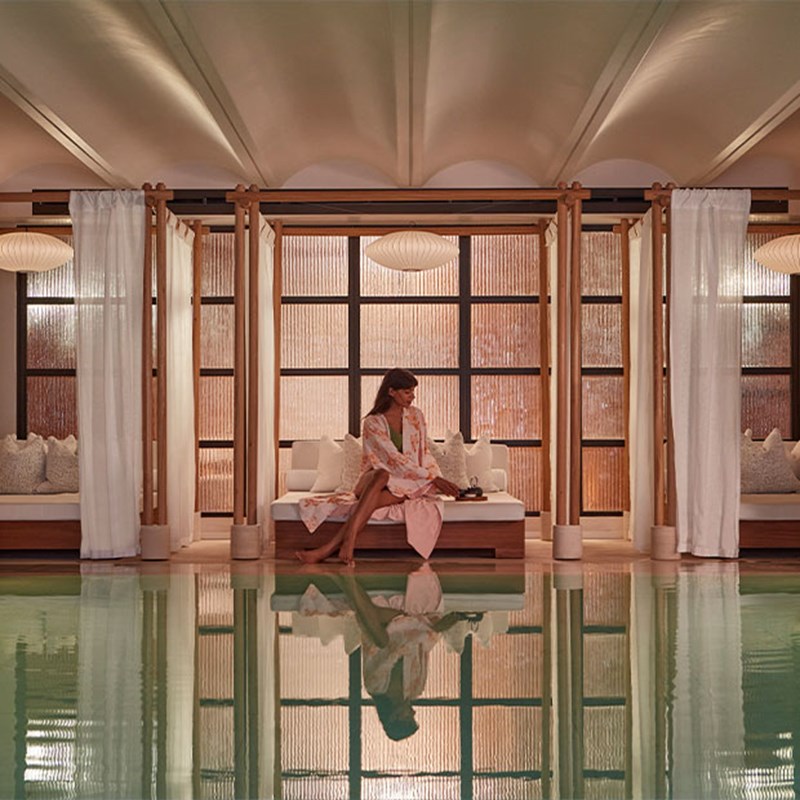 View of Claridge's Spa pool and at the end, a woman sat on a cabana in a pink printed kimono.