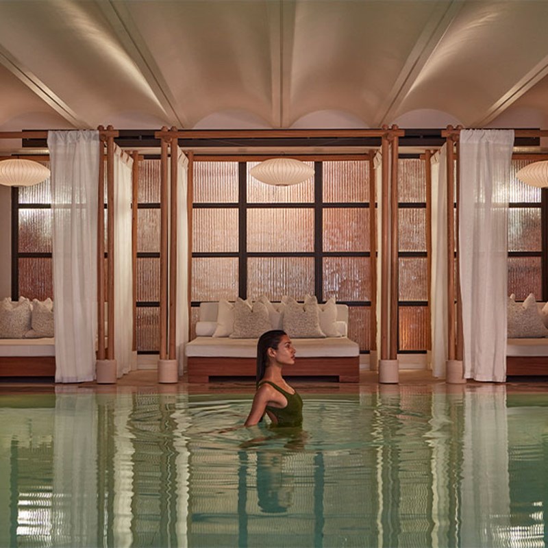 Claridge's Spa pool with a side on view of a lady with dark hair in a green swim suit. Behind is a cabana with cushions