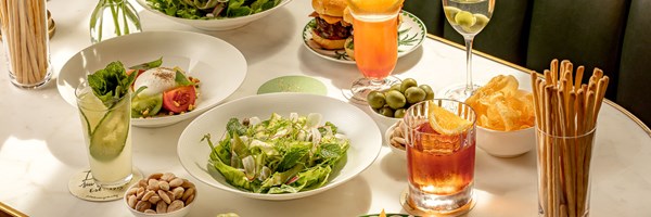 A marble table with salads, burrata with heirloom tomatoes, breadsticks, sliders, cocktails, olives, crisps, and almonds.