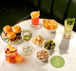 A marble table with sliders, cocktails, crisps, almonds, green olives, and cheese, set against a green banquette.