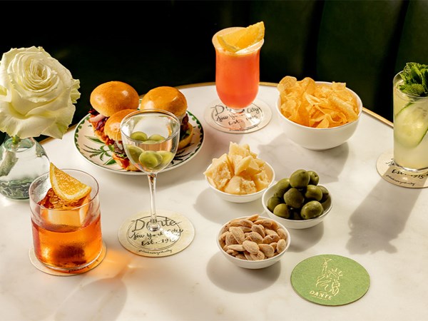 A close-up of a marble table with sliders, cheese, olives, crisps, almonds, and colorful cocktails.