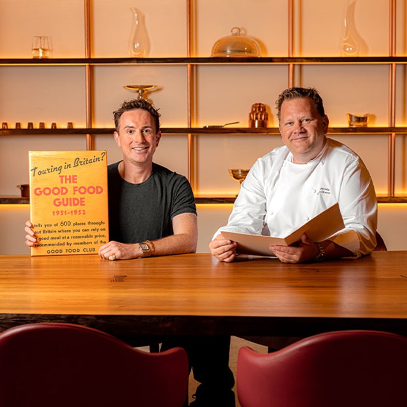 2 chefs sat holding up 'The Good Food Guide 1951-1952.'