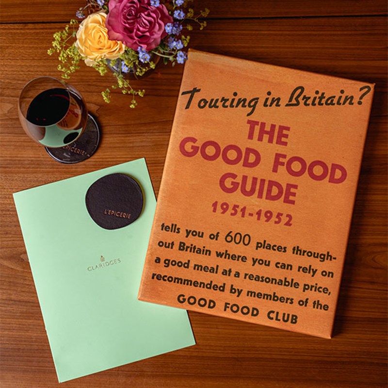 The Good Food Guide 1951-1952 beside a Claridge's menu, a small boquet of flowers and a glass of red wine.