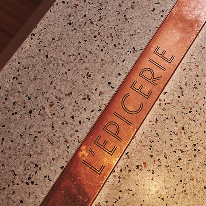 Brass plate on the floor with 'L'Epiciere' etched in aesthetic scribe.