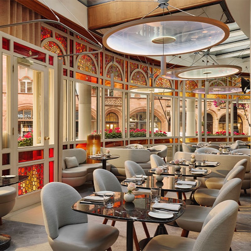 A contemporary restaurant with curved red and gold stained-glass windows, plush seating, and marble-top tables.